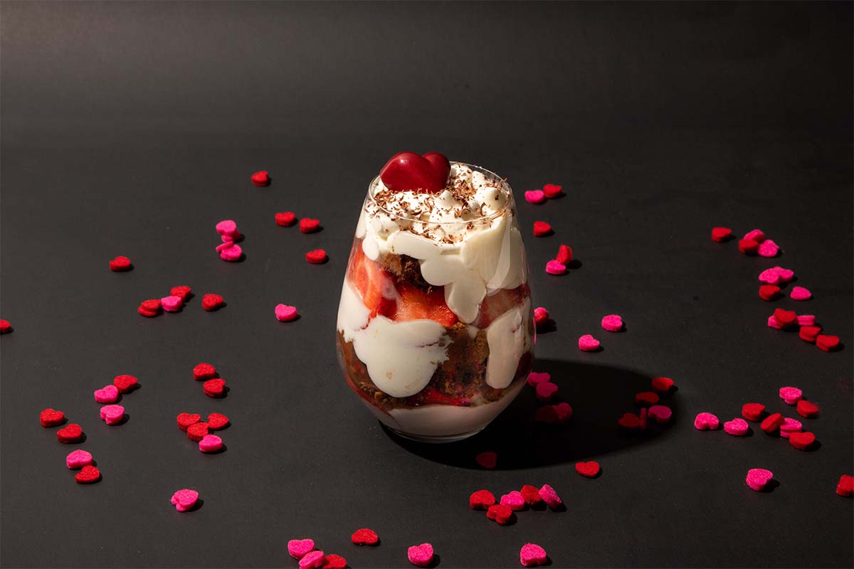 Image of heart shaped confetti surrounding a parfait with a cherry on top on a black background